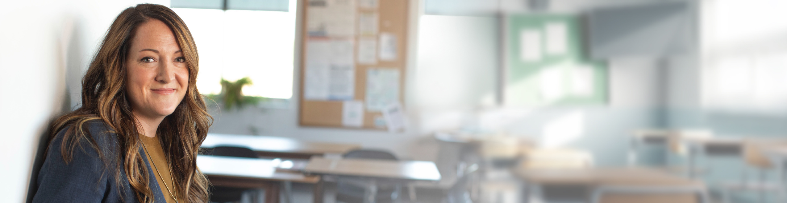 A woman leaned against a wall with a classroom behind her