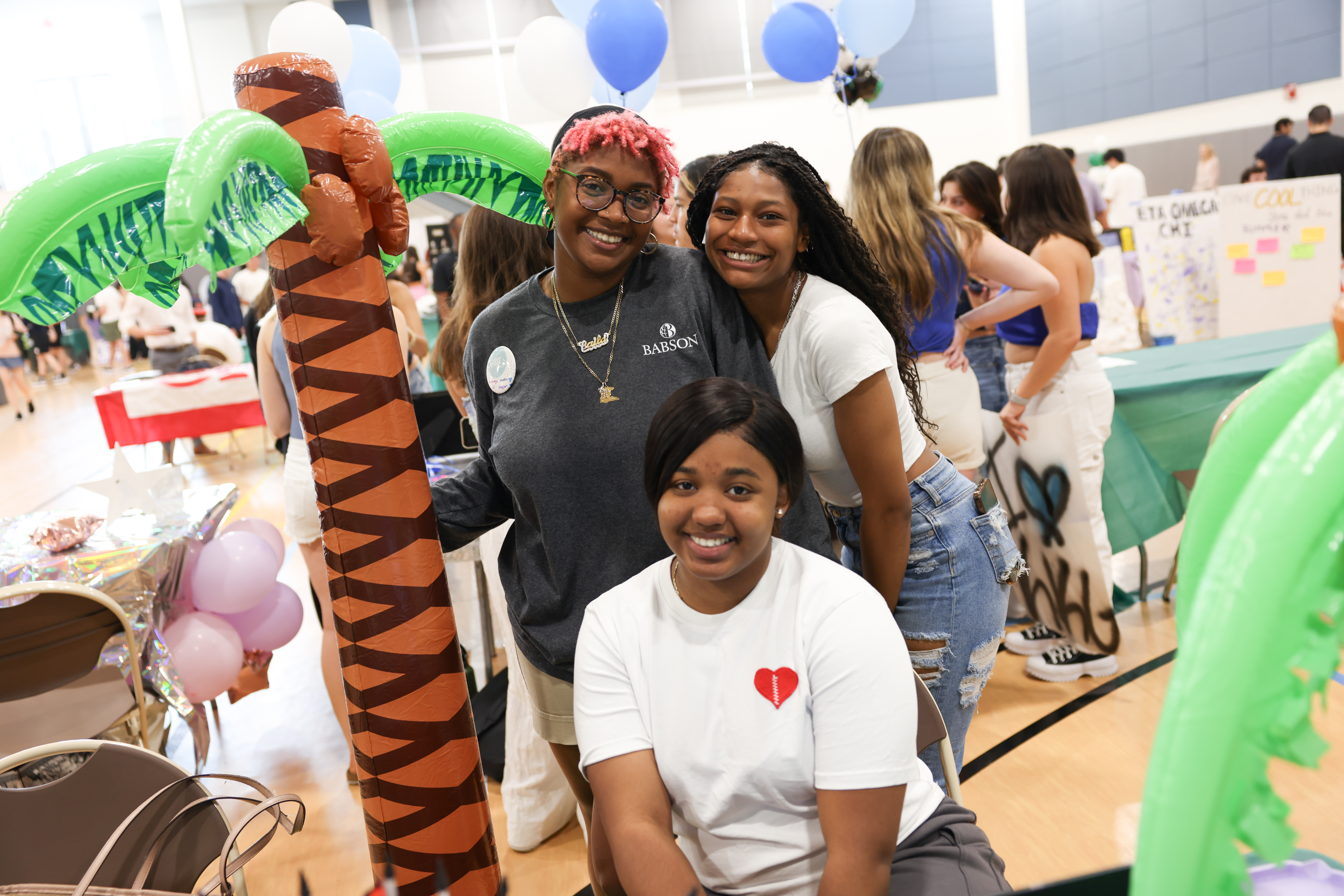 Three students and an inflatable palm tree at the club fair