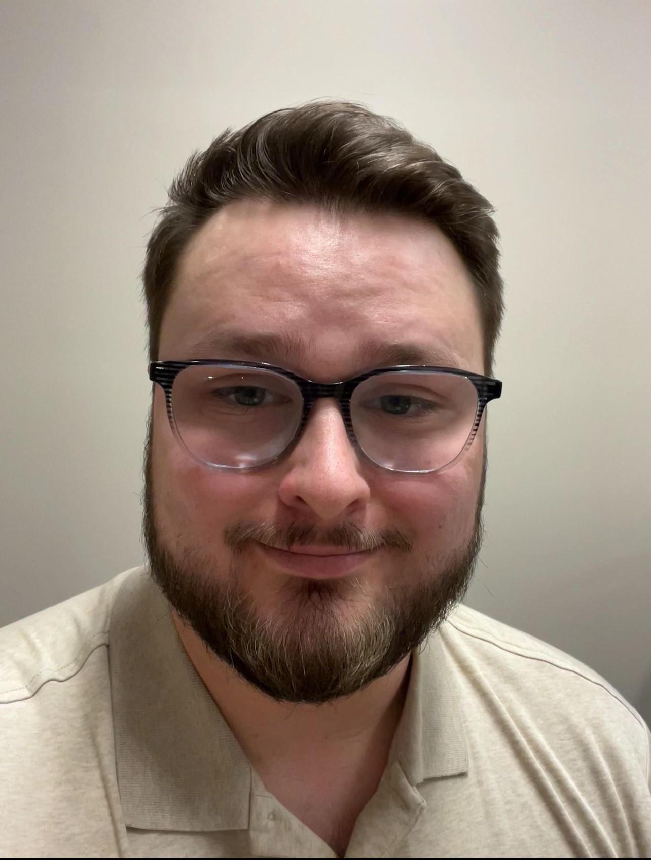 Charles has brown hair and is wearing a beige shirt with glasses in front of a beige background.